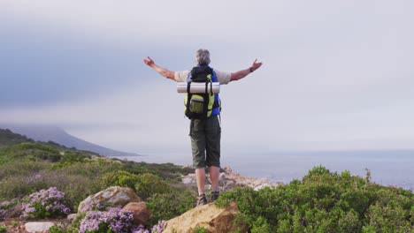 rear view of senior hiker man standing with his arms wide open standing on a rock