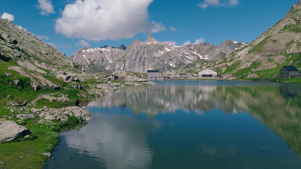 Lago alpino limpido che riflette montagne aspre e nuvole vicino al confine svizzero-italiano.