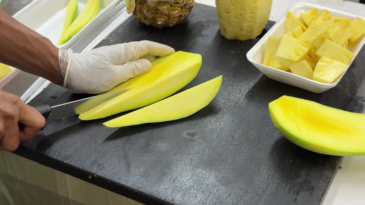 Chef che affetta mango fresco in pezzi uniformi su tagliere