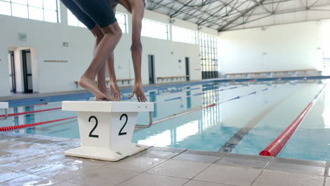 person stands on a starting block at a swimming pool