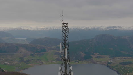 Primer-Plano-De-Un-Dron-Orbitando-Un-Mástil-De-Teléfono-5g-Con-Fondo-De-Montaña,-Escandinavia