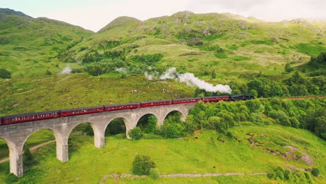 Aerial-of-Jacobite-Steam-Train-Crossing-Glenfinnan-Viaduct-Railway-Bridge,-Scottish-Highlands,-Scotland,-United-Kingdom