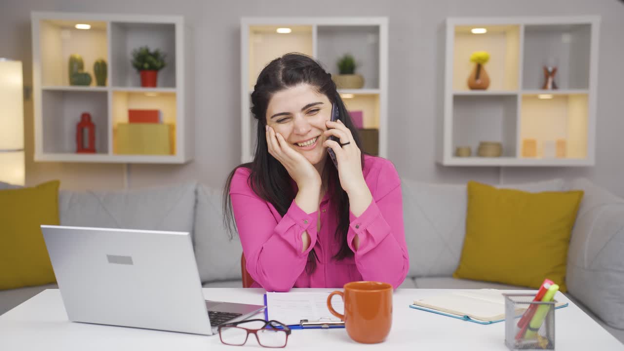 una mujer que trabaja en una oficina en casa se alegra por teléfono.