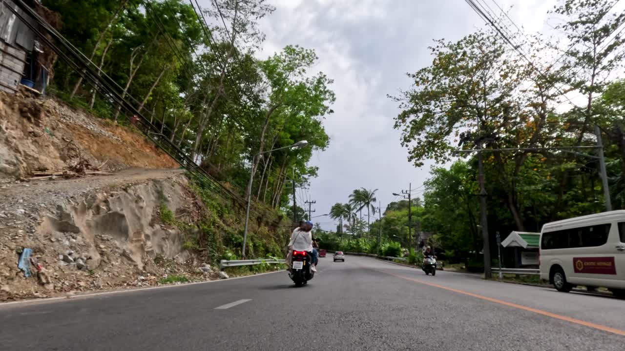 Motorbike travels on scenic, tree-lined road in Phuket, Thailand under natural daylight, wide perspective