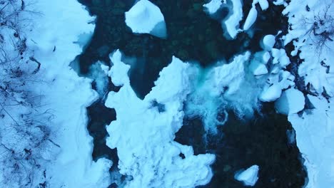 top view of creek in the wintertime with snow covered boulders as the aerial view rises above the scene