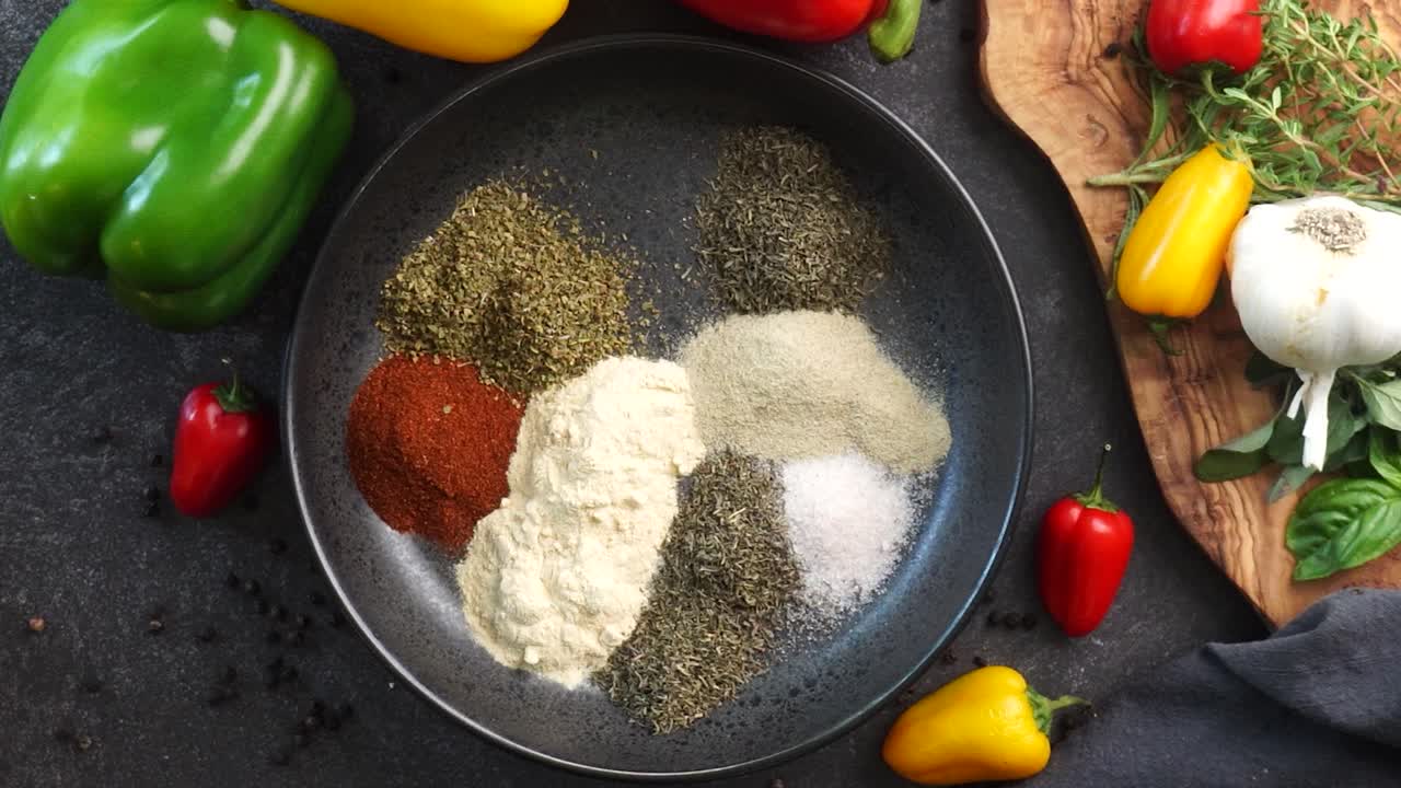 Making a vibrant Cajun Spice Blend, mixing red paprika, cayenne pepper, oregano, thyme, white garlic onion powder and black pepper in a bowl, creating a striking contrast against a black background.