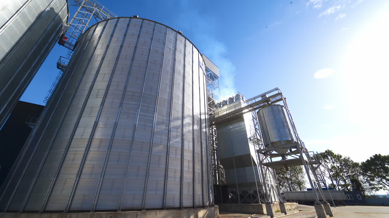 Modern grain elevators at bright sunny day. Large granary under blue sky. Industrial manufacturing in the open air.