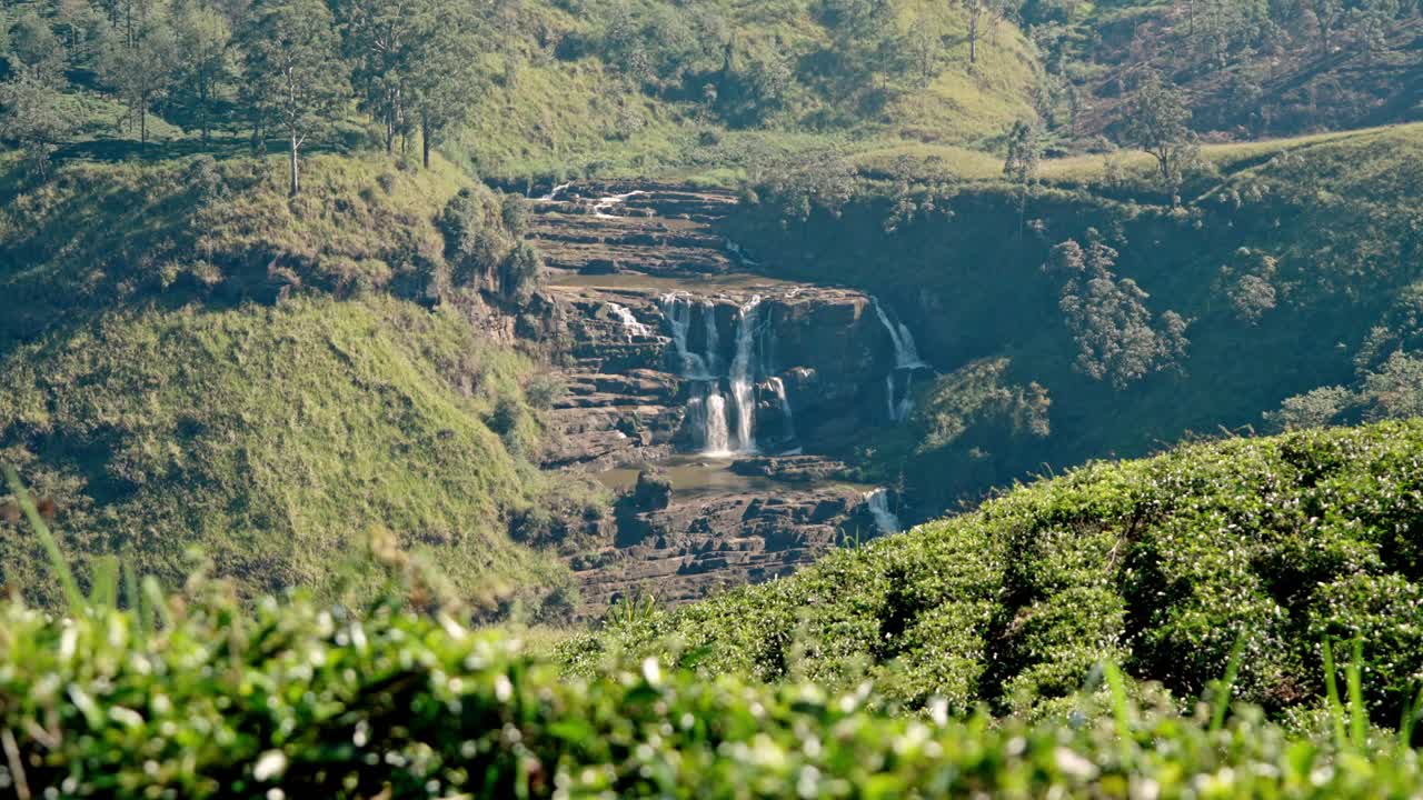 Footage of lush green tea plantations sprawling across the rolling hills of Nuwara Eliya, with the cascading waters of Saint Clair’s Falls visible in the background.