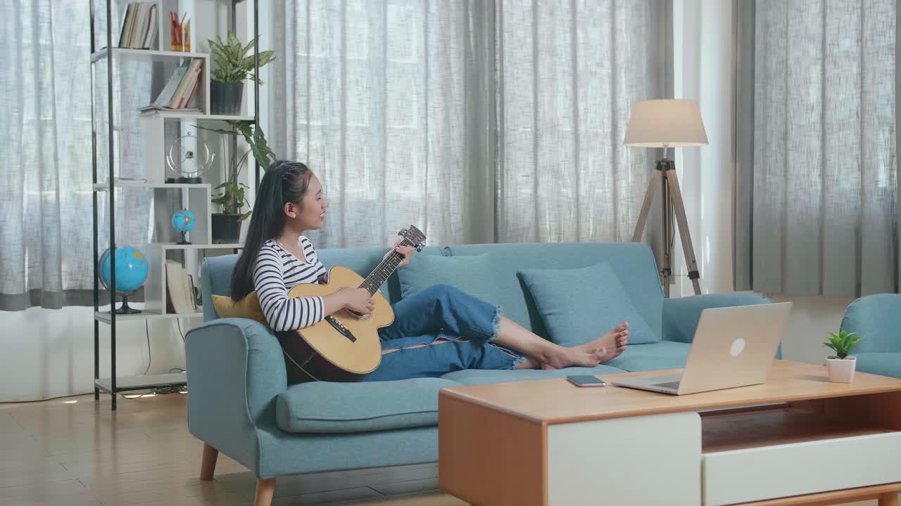 집에서 소파에서 어쿠스틱 기타를 연주하는 여자