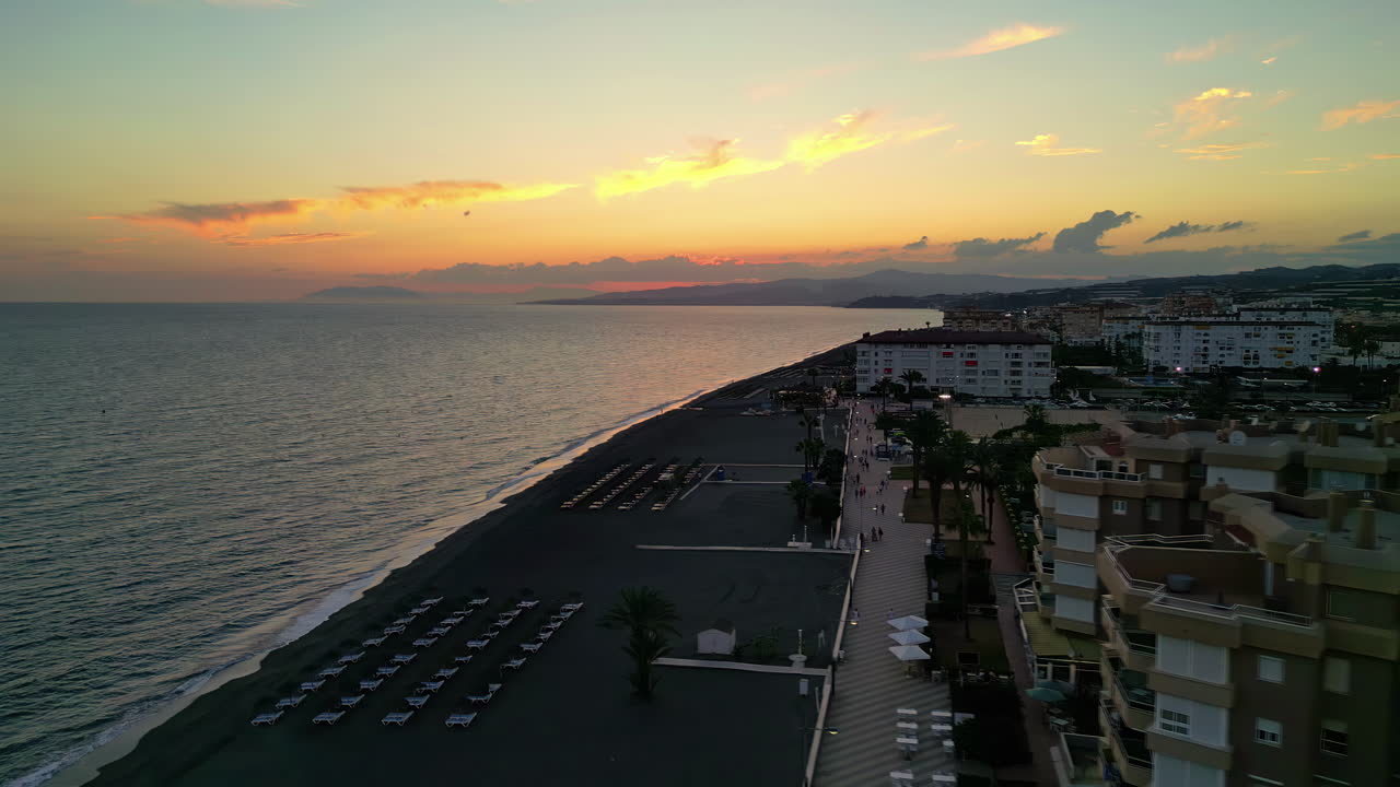 Lettini prendisole e hotel fronte mare al tramonto a Playa de Torrox a Malaga, Spagna.