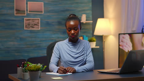 Black-business-woman-writing-in-notebook-working-overtime