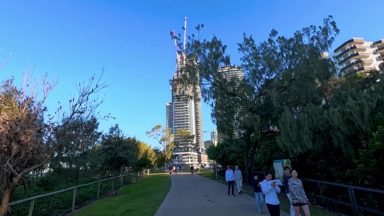 Ripresa in carrello grandangolare lungo un sentiero costiero soleggiato verso i grattacieli di Surfers Paradise, Queensland.