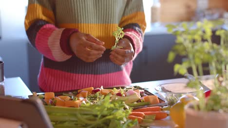 Mid-section-of-african-american-woman-preparing-meal-using-tablet-in-sunny-kitchen