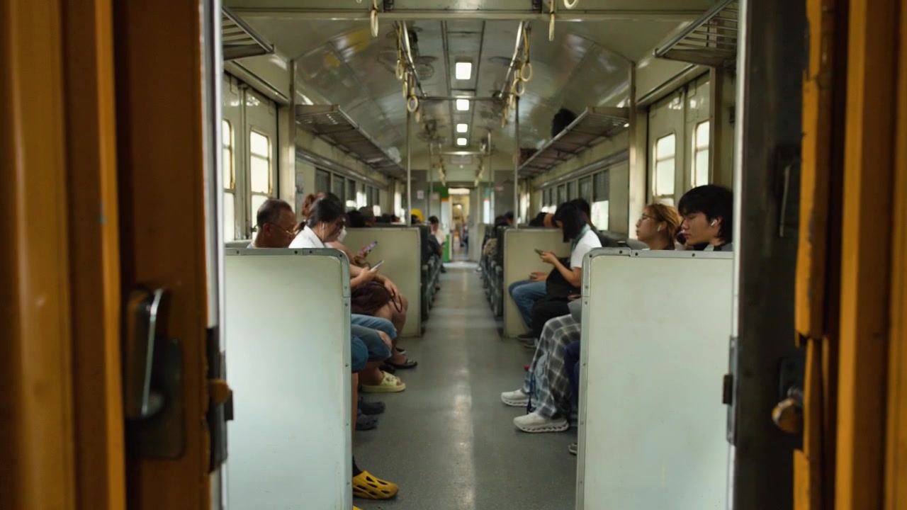 Camera moves through sliding doors into a train car filled with seated passengers commuting.