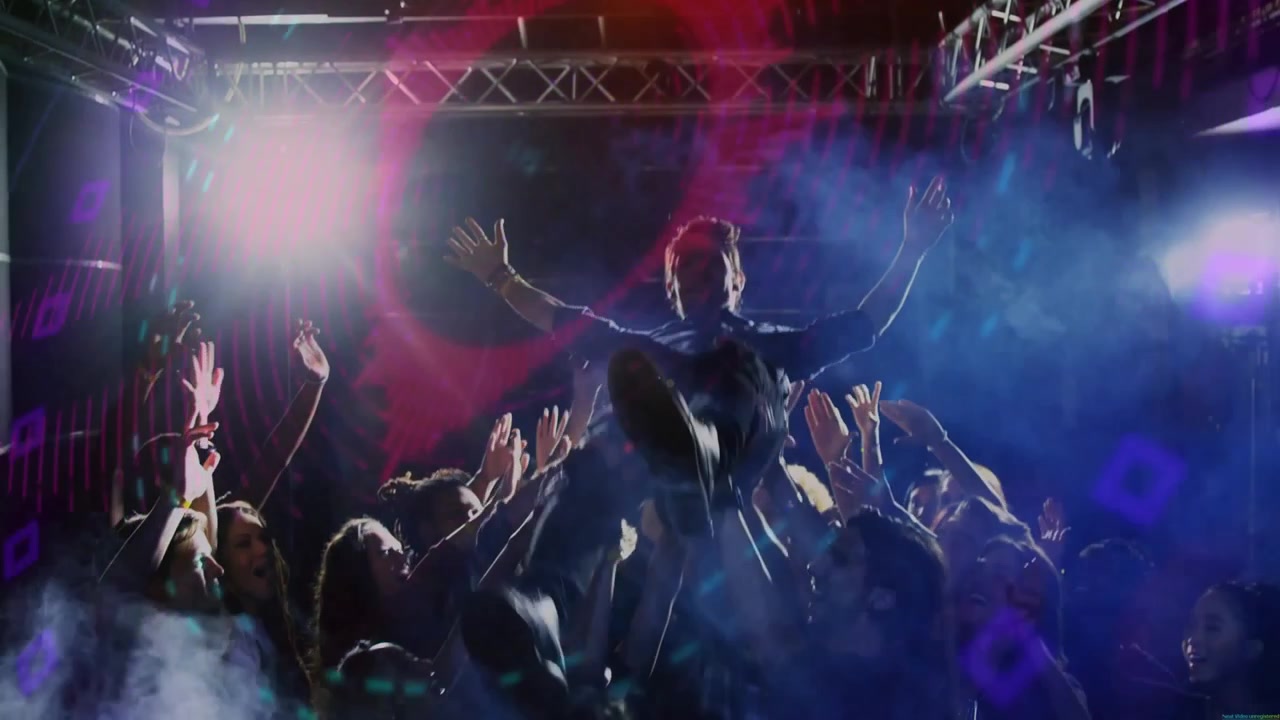 Artist kliver upp på scen, höjer armarna och peppar musikfans som crowdsurfar under färgade ljusstrålar.