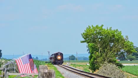 a train travels down the tracks surrounded by lush farmland and a distant view of rolling hills