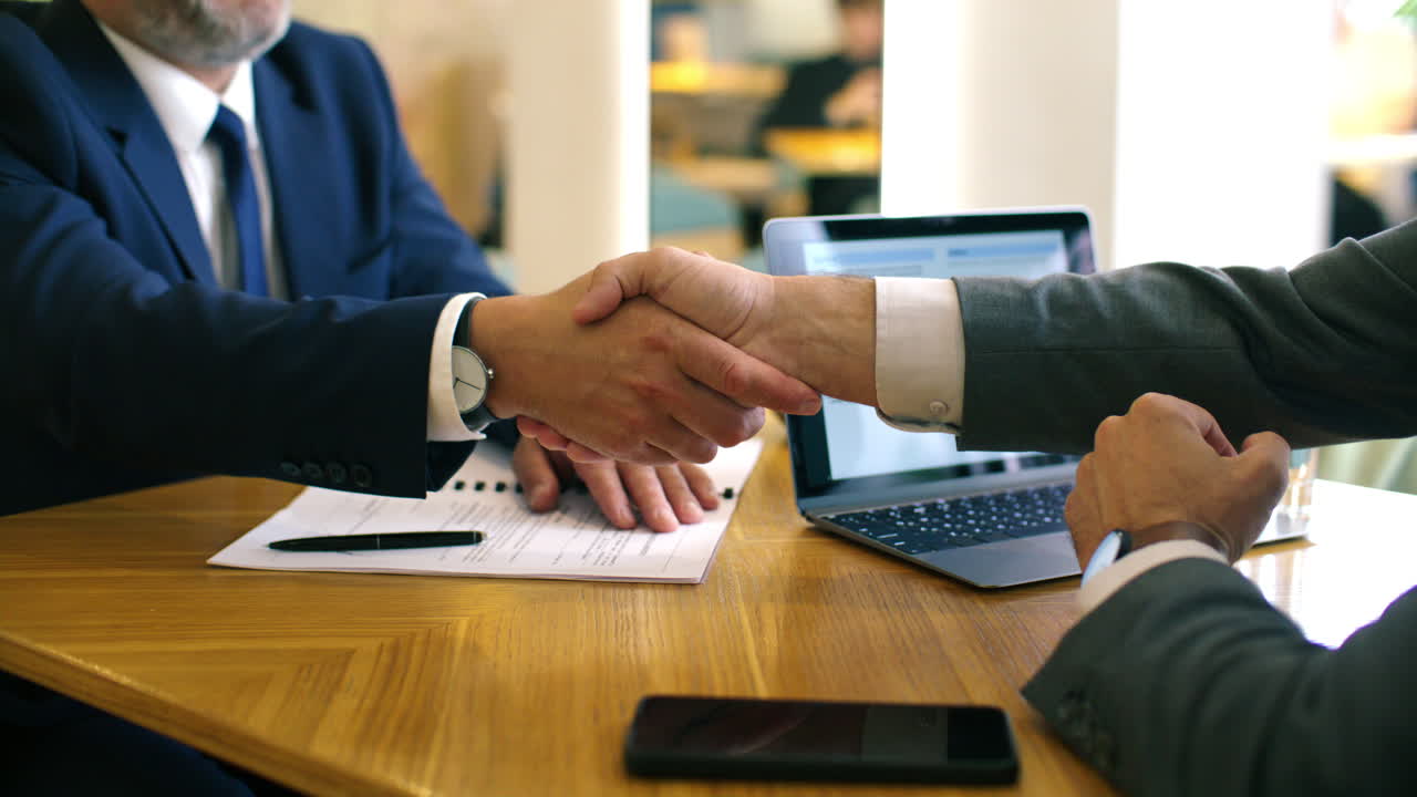 Close Up of Two Businessmen Shaking Hands after Signing Contract in Cafe