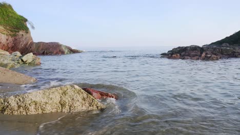 Gentle-beach-waves-around-rocks-on-a-sunny-day-in-Talland-Bay,-Cornwall