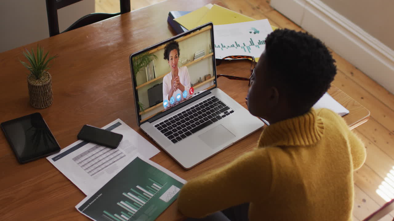 mujer de negocios afroamericana sentada en un escritorio usando una computadora portátil haciendo una videollamada con un colega