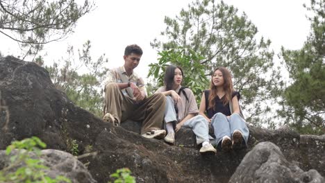 young asian indonesian friends chatting and laughing on rocky hilltop in nature