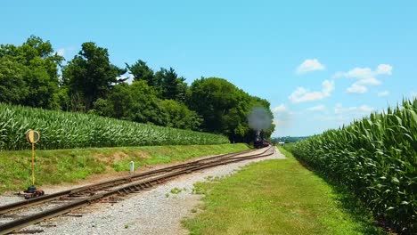 Schöner-Sonniger-Tag-Mit-Maisfeldern,-Blauem-Himmel-Und-Wenigen-Wolken-Und-Einer-Antiken-Dampflokomotive,-Die-Sich-Nähert