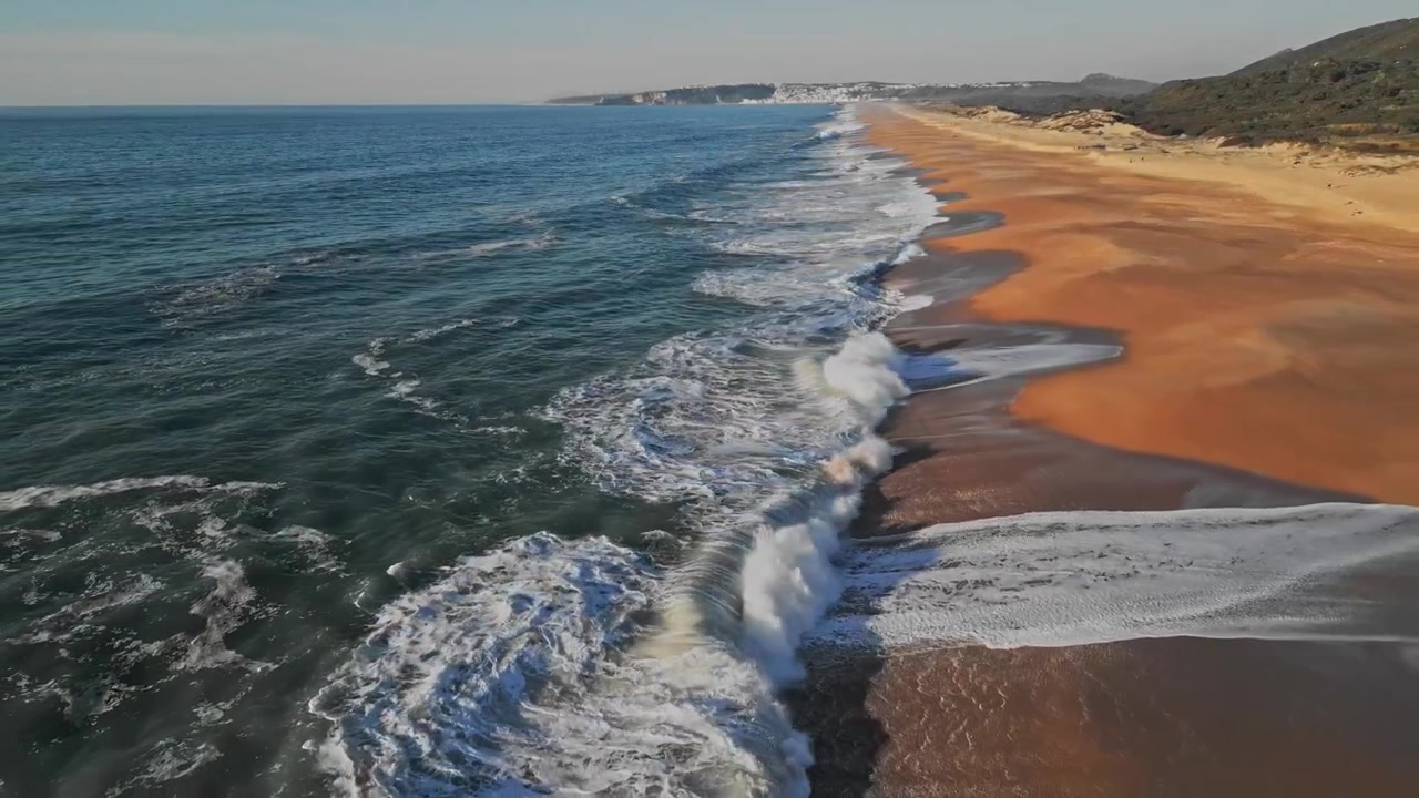 De pittoreske gouden kustlijn en beukende golven bij Praia do Salgado nabij Nazaré, Portugal, een cinematische slow motion luchtopname.