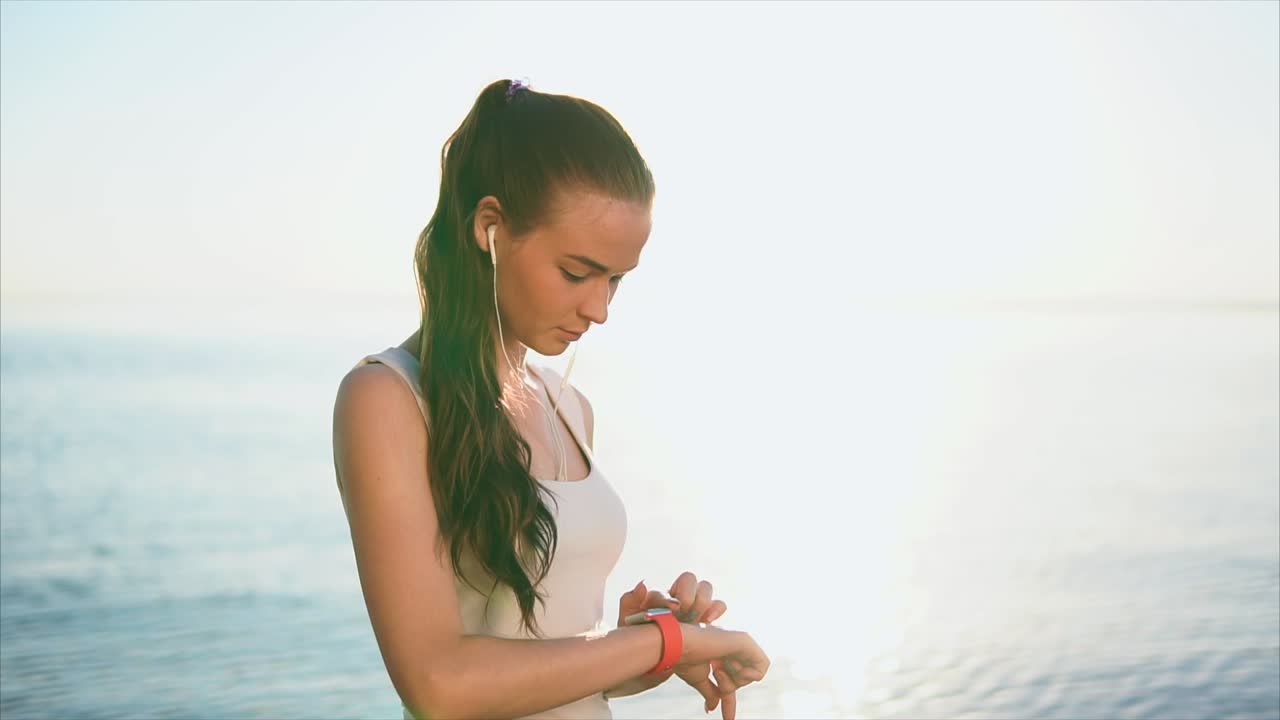 Woman listening to music and checking her smartwatch at the beach