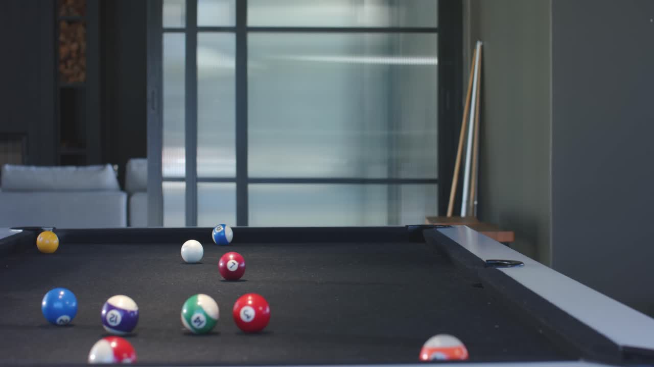 Senior African American female lining up shot, striking cue ball in game room, scattering balls