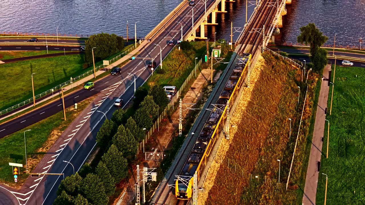 Aerial view of train on tracks at sunset, with roads and lush greenery