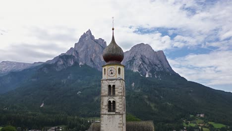 wonderful church tower in a valley on a green meadow with high mountains in the background, dolomites, italy, europe, drone