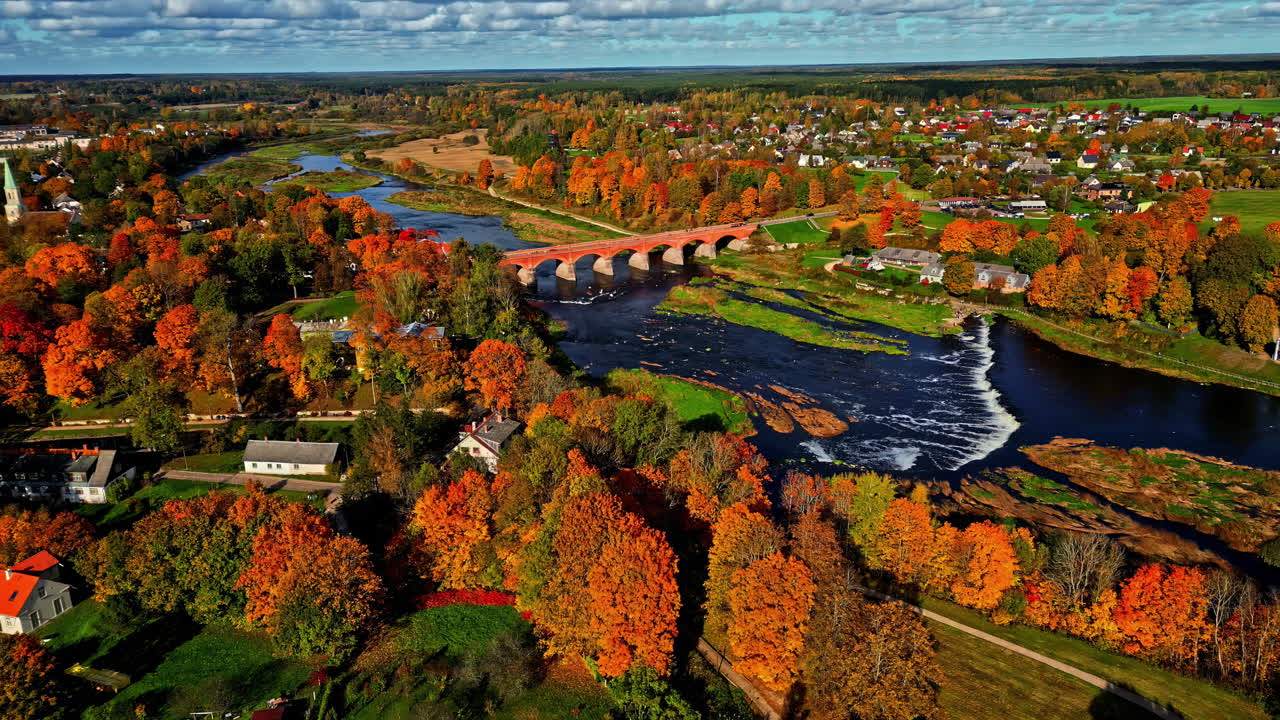 Autumn aerial view of Venta river with iconic rapid waterfall and brick bridge