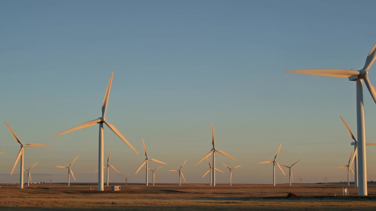 Fila di turbine eoliche che generano energia rinnovabile in un paesaggio pianeggiante sotto un cielo limpido al crepuscolo.