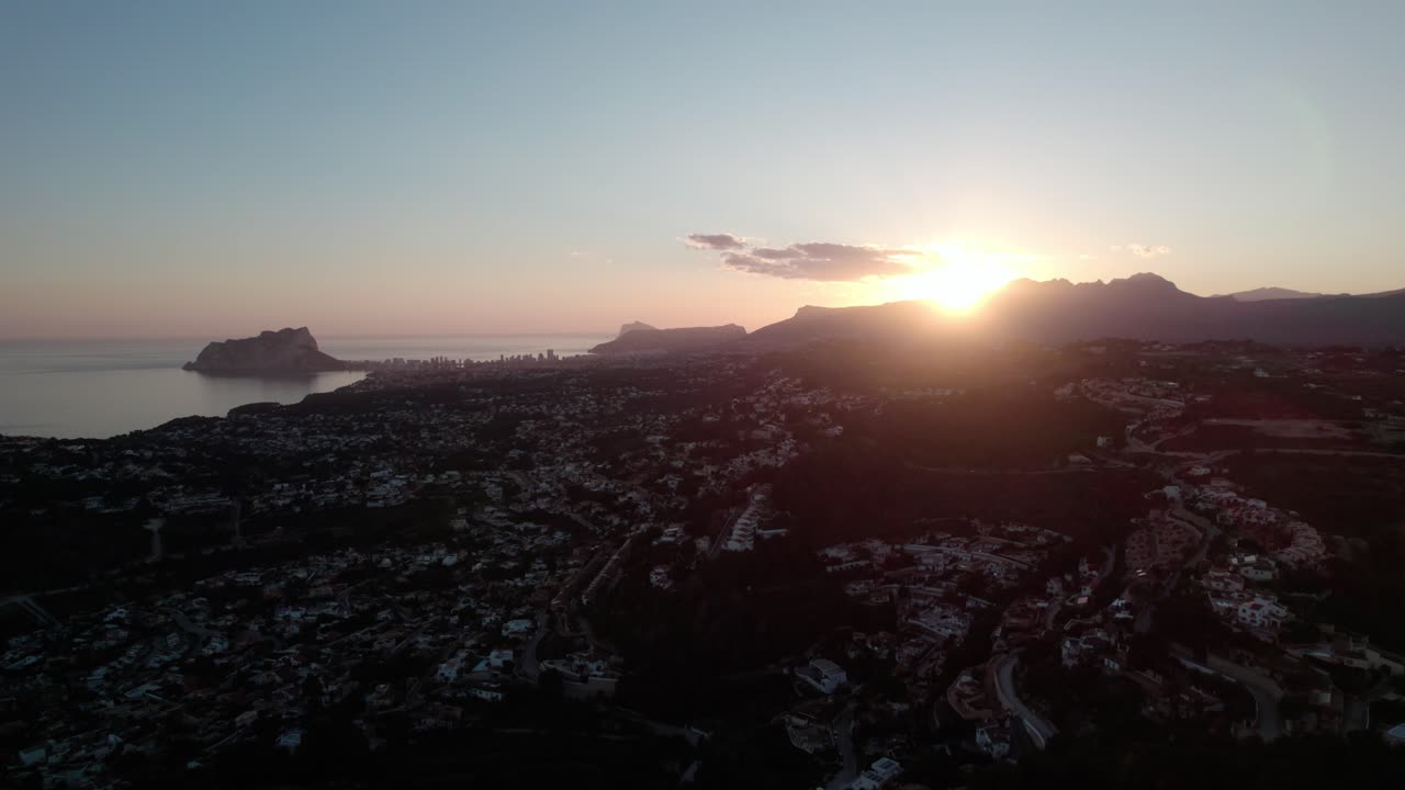 Aerial View Of Coastal Town In Alicante, Spain At Sunset, With Sun Behind Mountain Peaks In Distance. wide shot