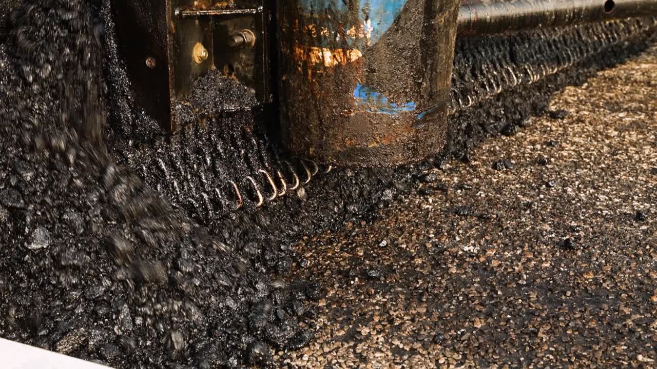 Asphalt paver machine working during the day, close-up shot. Road construction