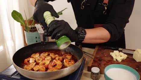 un chef profesional con guantes negros, condimentando los camarones con sal, agregando sabores y umami al delicioso plato de marisco con paprika