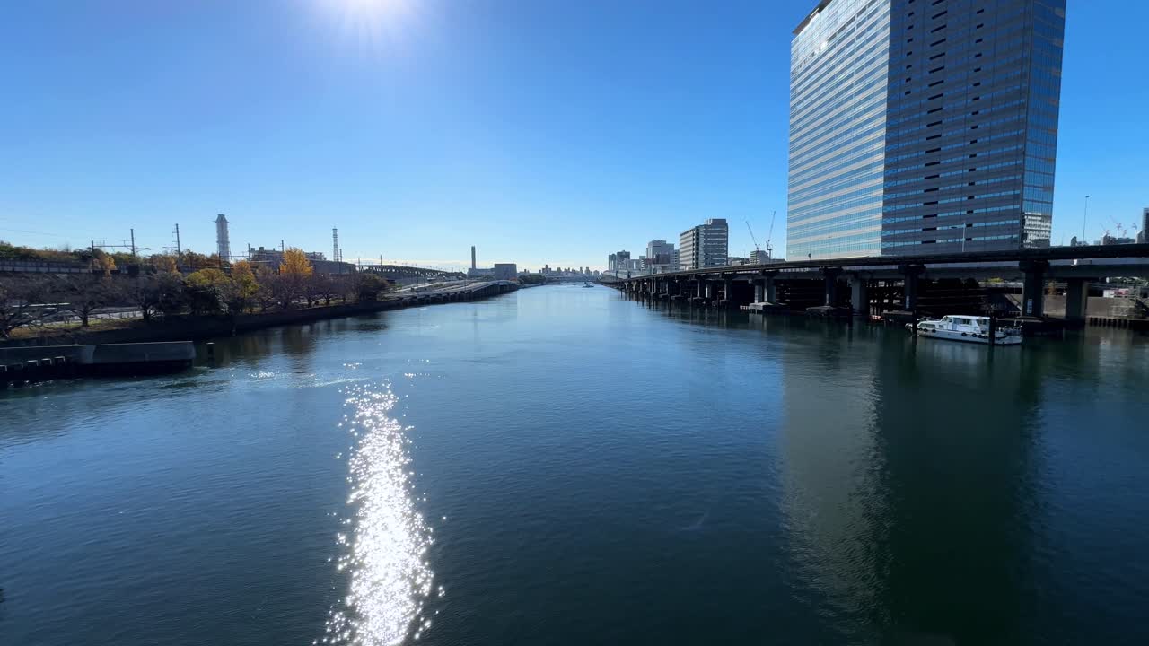 밝은 파란 하늘, 현대적인 도쿄 건물, 그리고 빛 반사와 함께 평온한 강 풍경