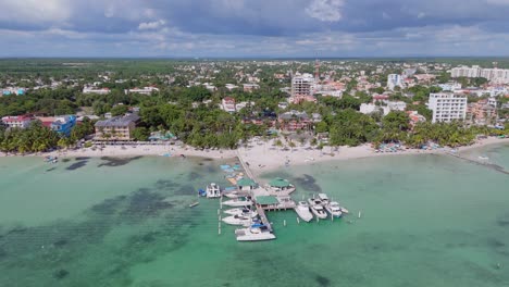 aerial orbiting shot of sandy boca chica beach with jetty and docking boats in santo domingo city at sunny day