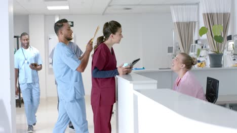 diverse doctors talking to medical receptionist sitting at front desk at hospital, slow motion