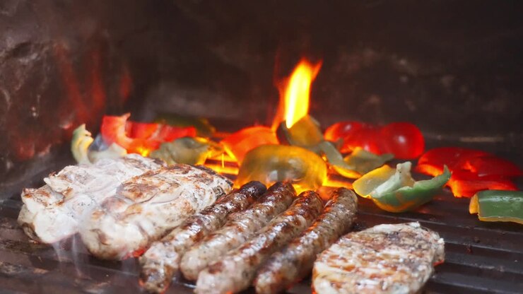 Grilled meat and vegetables sizzling on the barbecue with flames in the background