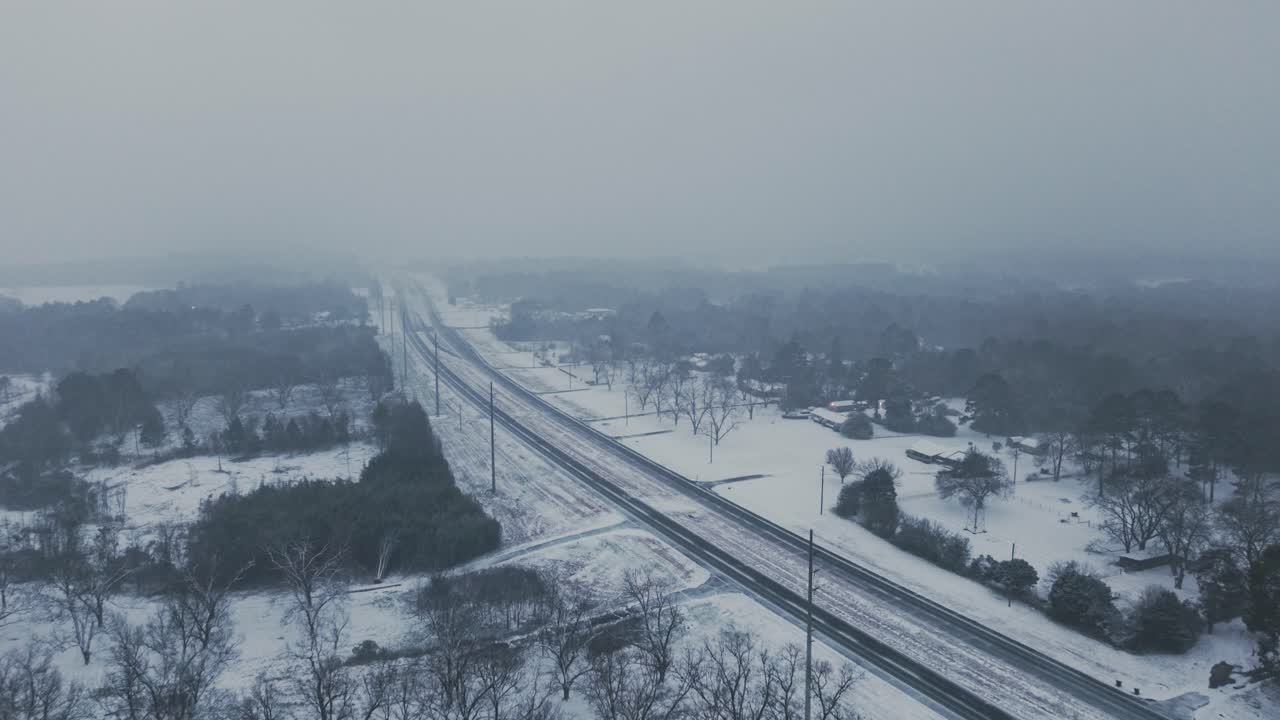 Drone captures a serene aerial view of a Georgia highway and surrounding landscape during a rare snowfall event. The soft snow blankets the road and countryside.