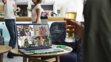 persona en un bar usando una computadora portátil haciendo una videollamada del día de san patricio con amigos en otro bar