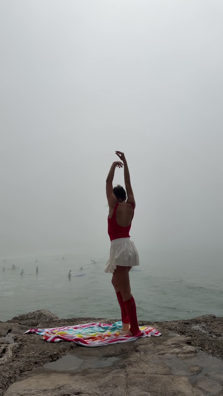 Giovane donna che balla il balletto su una costa rocciosa nella nebbia.