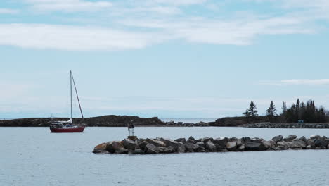 Red-sailboat-in-calm-harbor-against-a-blue-sky
