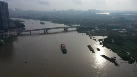 Early-morning-high-drone-view-looking-down-on-river-modern-traffic-bridge-and-boats-transporting-shipping-containers-and-building-materials