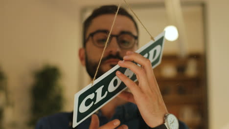 close-up view of young man turning over closed" sign in his coffee shop window"