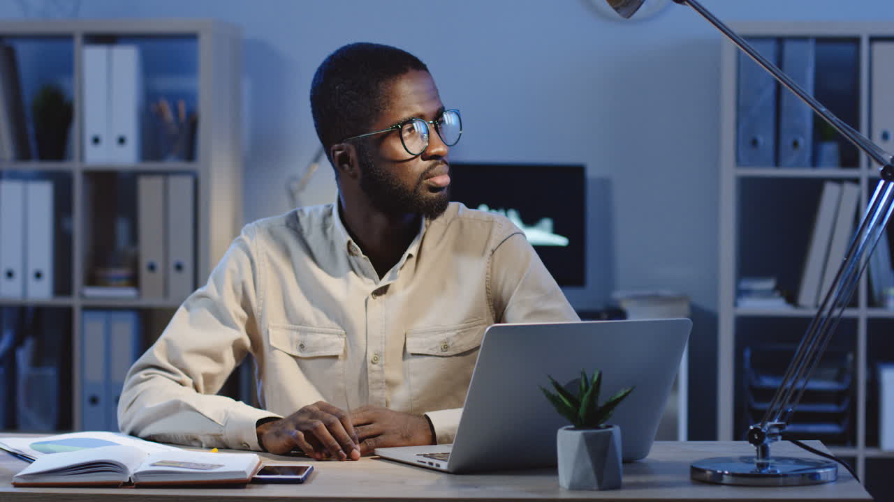Young Office Worker Sitting At The Office Desk Looking And Smiling At Camera In The Office At Night