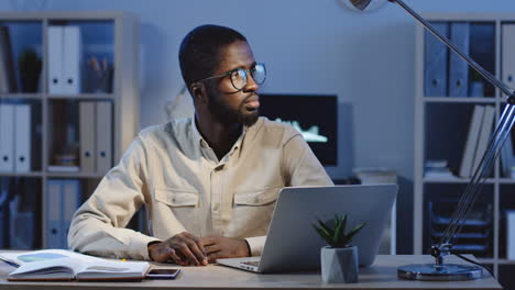 young office worker sitting at the office desk looking and smiling at camera in the office at night