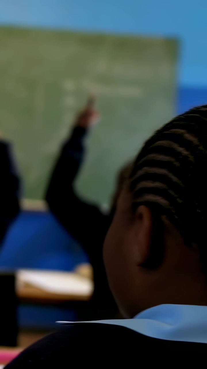 Vídeo vertical: Observando menino de uniforme na aula, professor perguntando no quadro, alunos levantando as mãos.