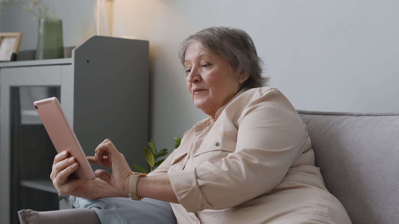 Smiling Senior Woman Using Tablet While Lying On Sofa At Home