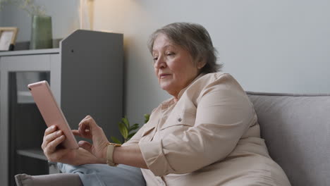 smiling senior woman using tablet while lying on sofa at home